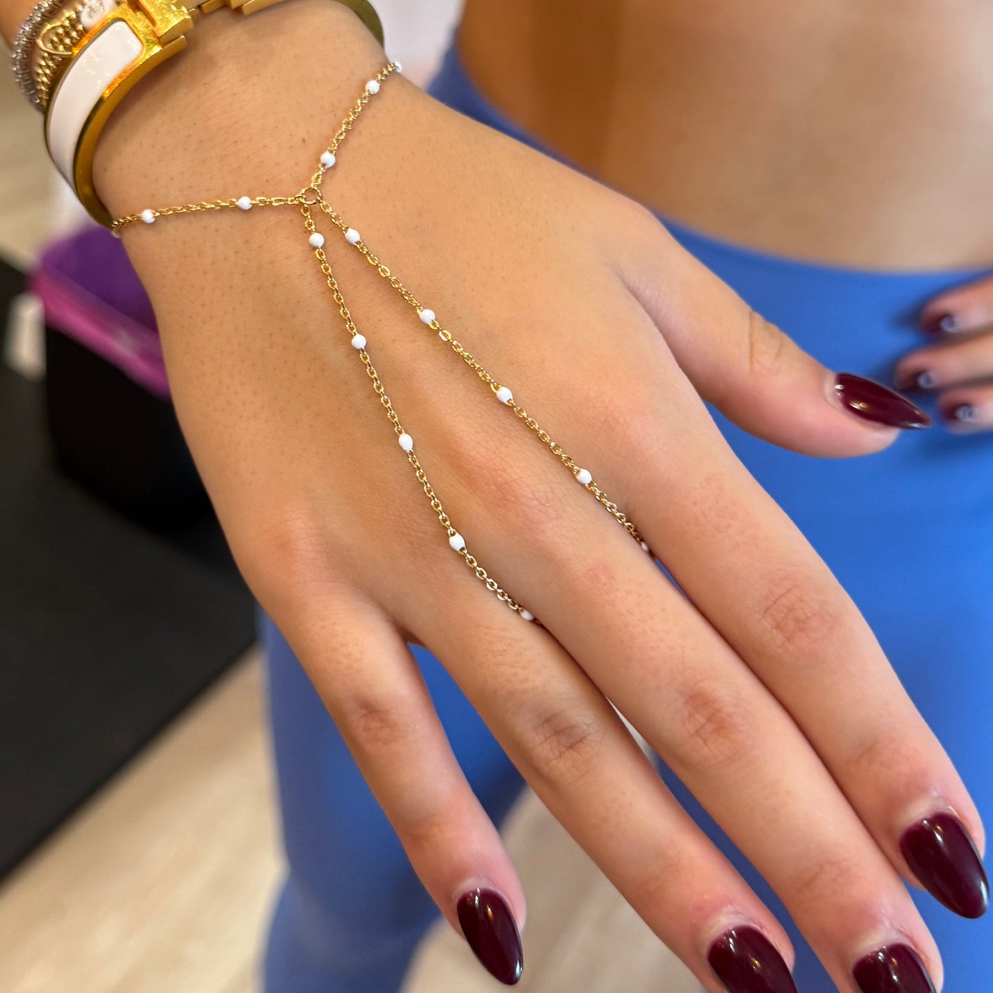 Close-up of a hand with gold bracelets and red nail polish, wearing a blue top.
